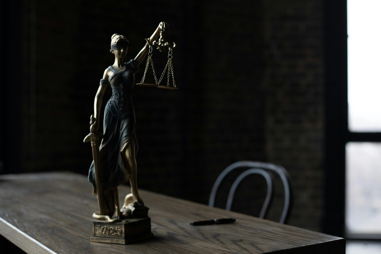 Lady Justice figurine on wooden table in dimly lit room symbolizes law and fairness.